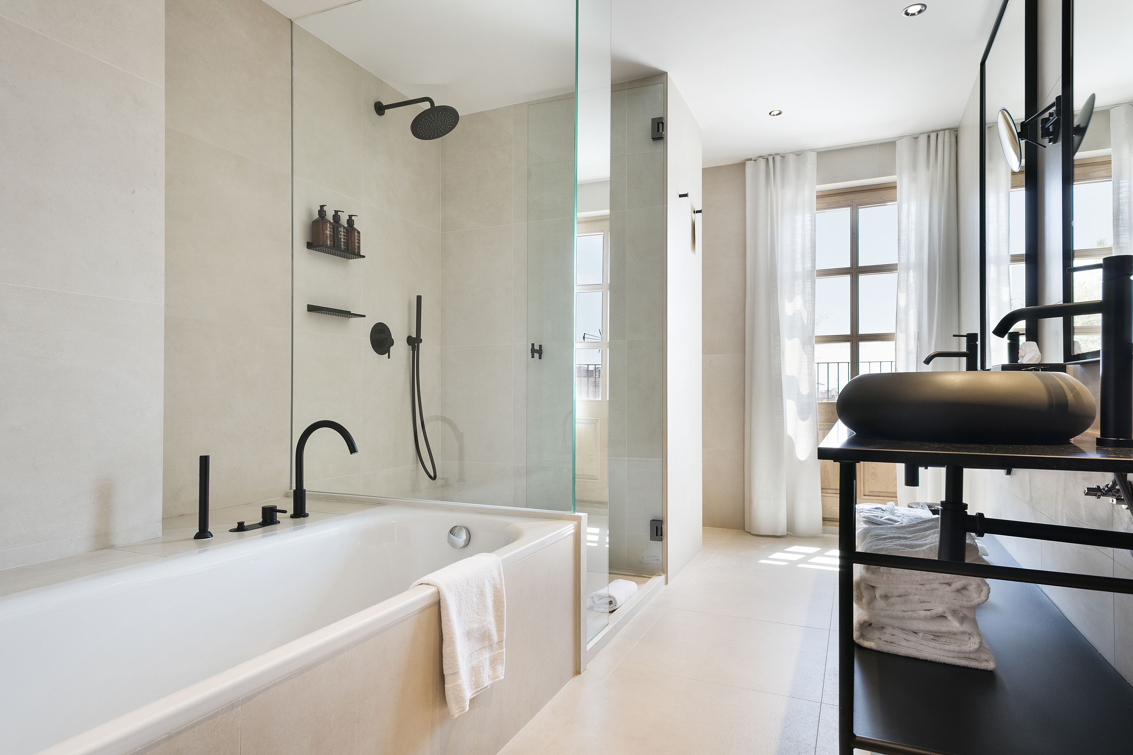 Une salle de bain moderne avec une baignoire, une douche à l’italienne en verre et un meuble-lavabo doté d’un plan de toilette noir.