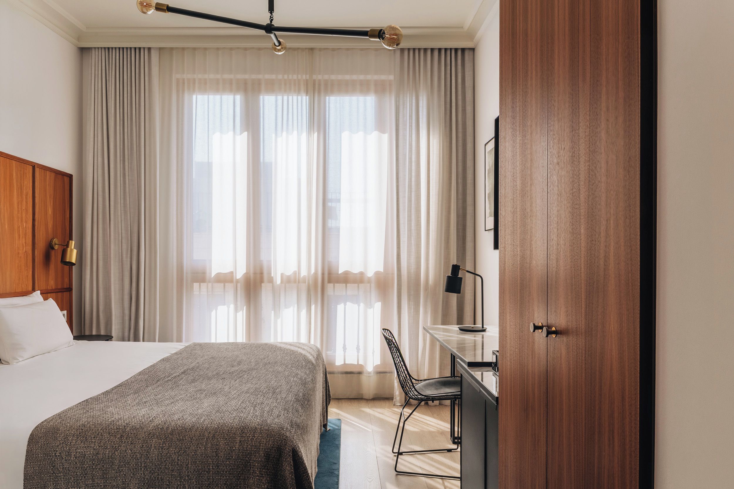 A hotel room with a bed, a desk, a chair, and a wardrobe.
