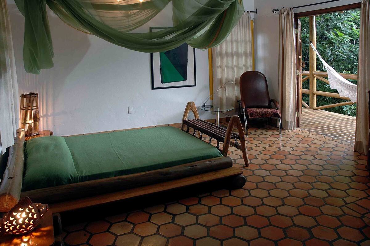 A room with a bed, a chair, a hammock, and a view of greenery outside.