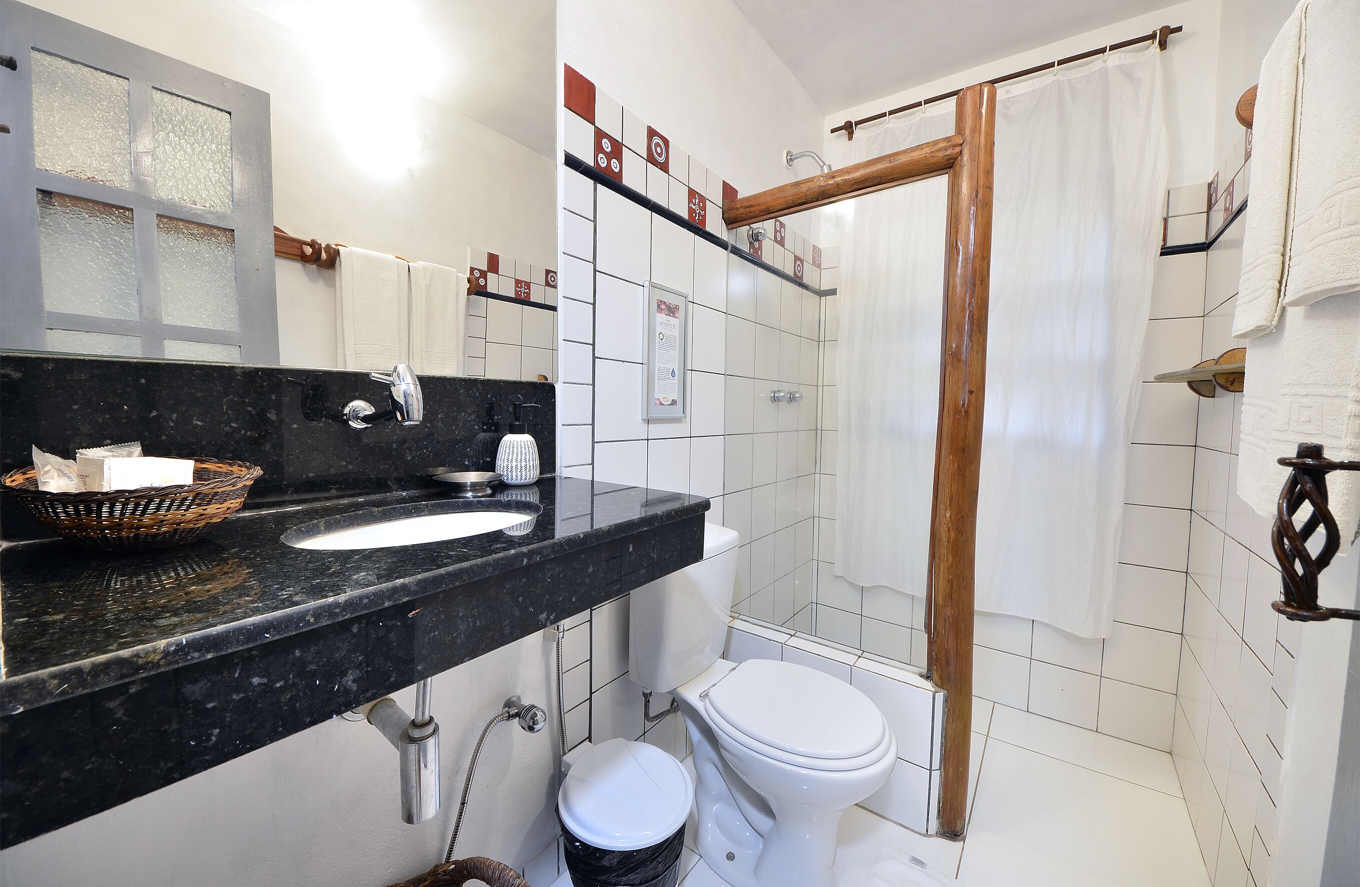 Un baño con lavamanos de mármol negro, inodoro blanco y zona de ducha con estructura de madera.