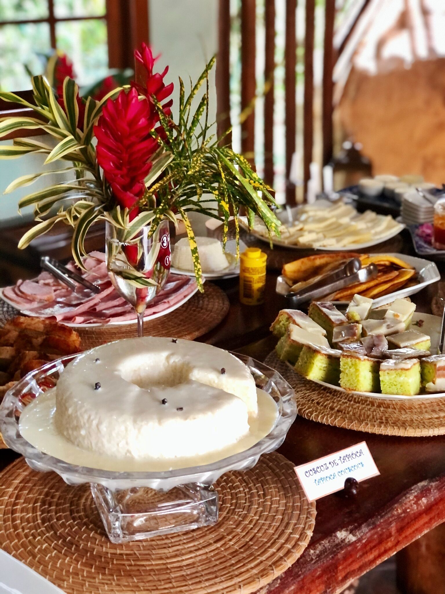 Een buffet met diverse gerechten, waaronder een taart met een etiket, en een decoratieve bloemstelling met rode bloemen en groene bladeren.