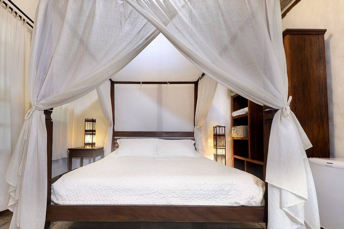 A four-poster canopy bed with a wooden frame and white bedding.