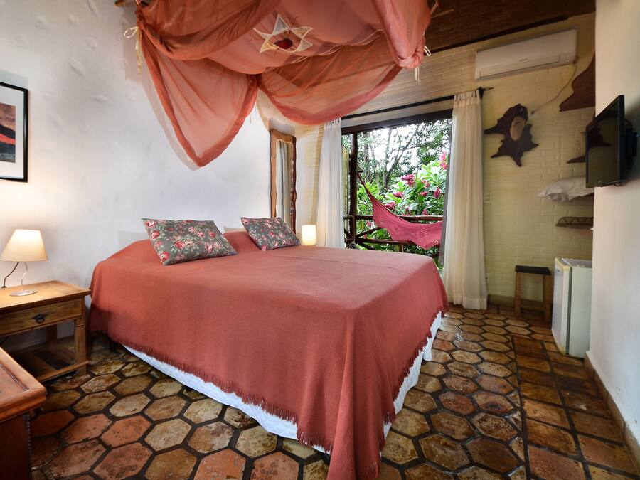 Un dormitorio con cama, mesita de noche, lámpara, televisor y vista a zonas verdes.