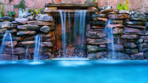 Une cascade artificielle en pierre, avec de l’eau qui s’écoule sur des rochers et se déverse dans un bassin.