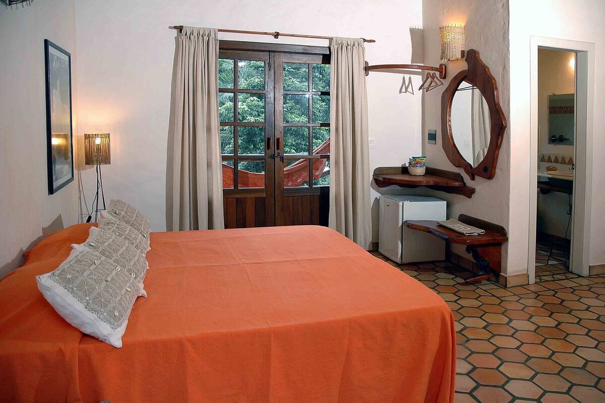 A bedroom with a bed, a desk, a mirror, and a window with curtains.