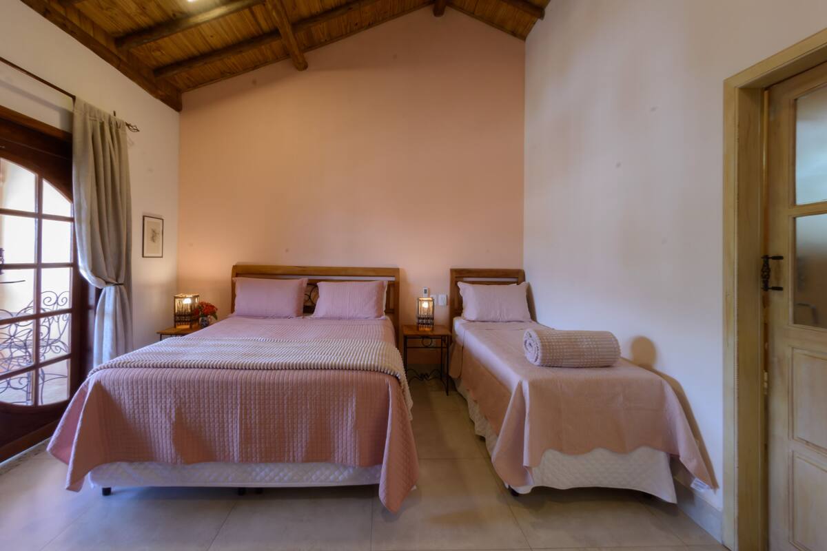 A bedroom with two beds, a window with curtains, a nightstand with a lamp, and a door.