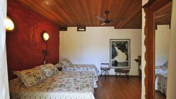A room with two beds, wooden ceiling, a ceiling fan, a framed picture on the wall, and a small table with a chair.