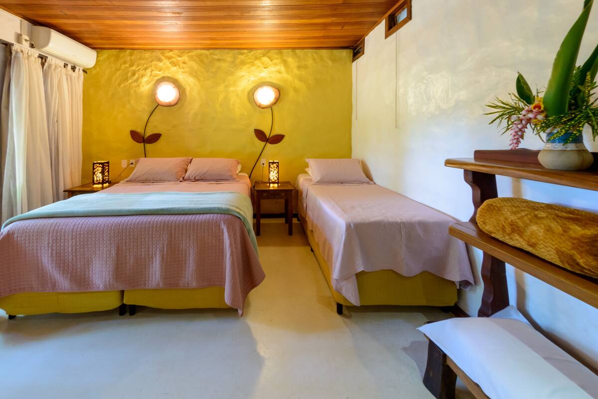 A room with two beds, a wooden ceiling, a wall-mounted air conditioner, and a bedside table with a lamp.