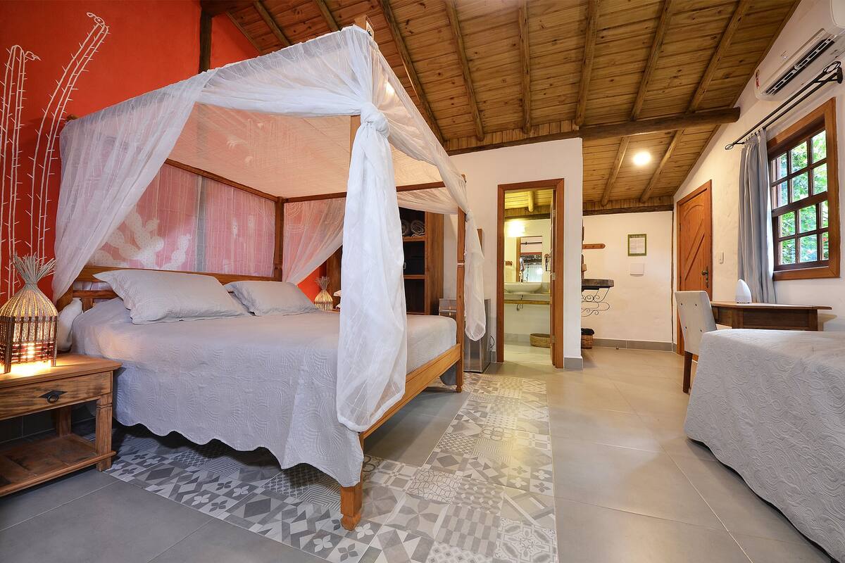 A bedroom with a canopy bed, a nightstand with a candle, and a patterned floor.