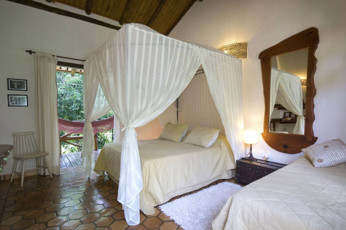 A bedroom with two beds, a wooden headboard, a nightstand, a mirror, and a window with curtains.