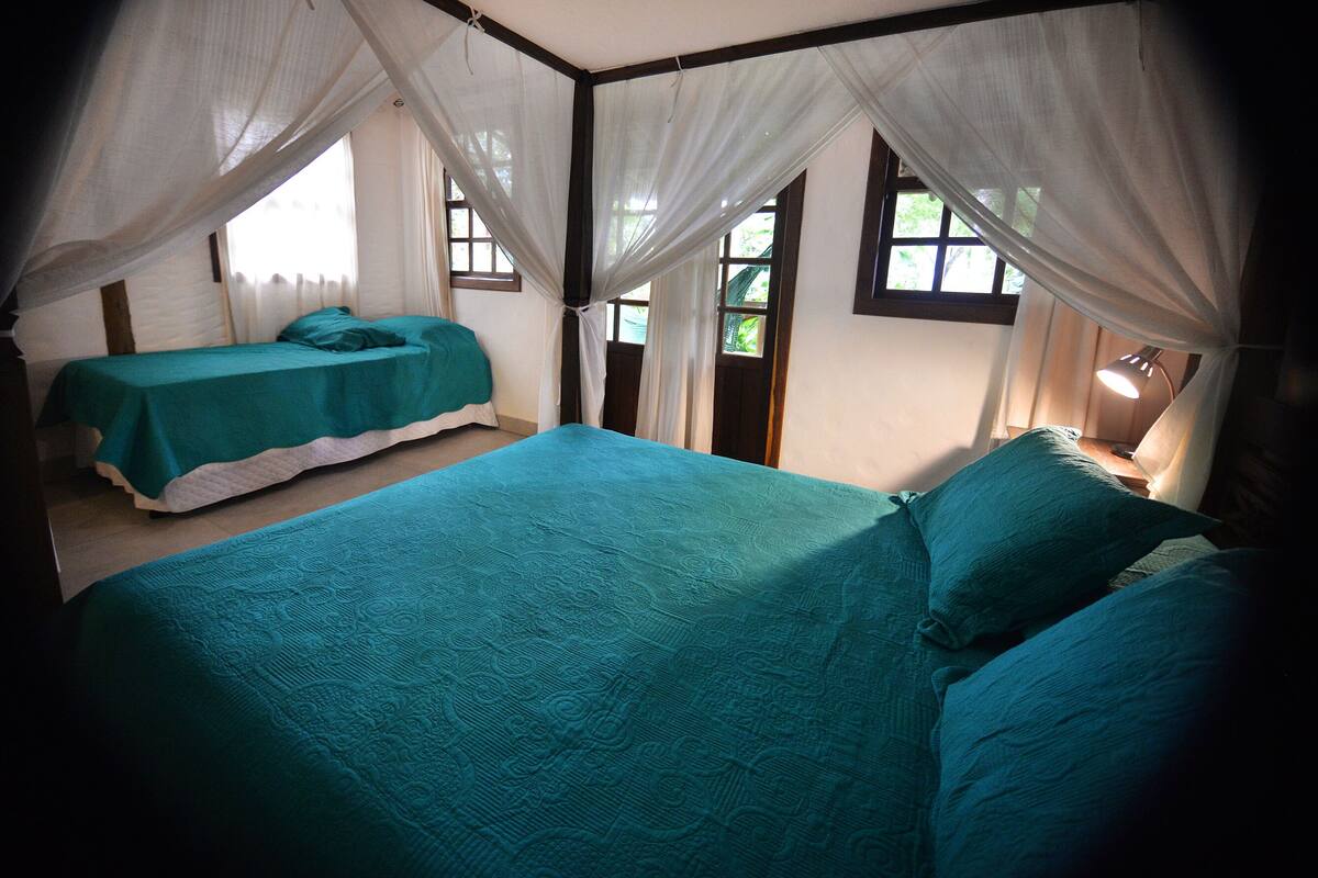 A room with two beds, each with a teal bedspread, and a canopy bed.