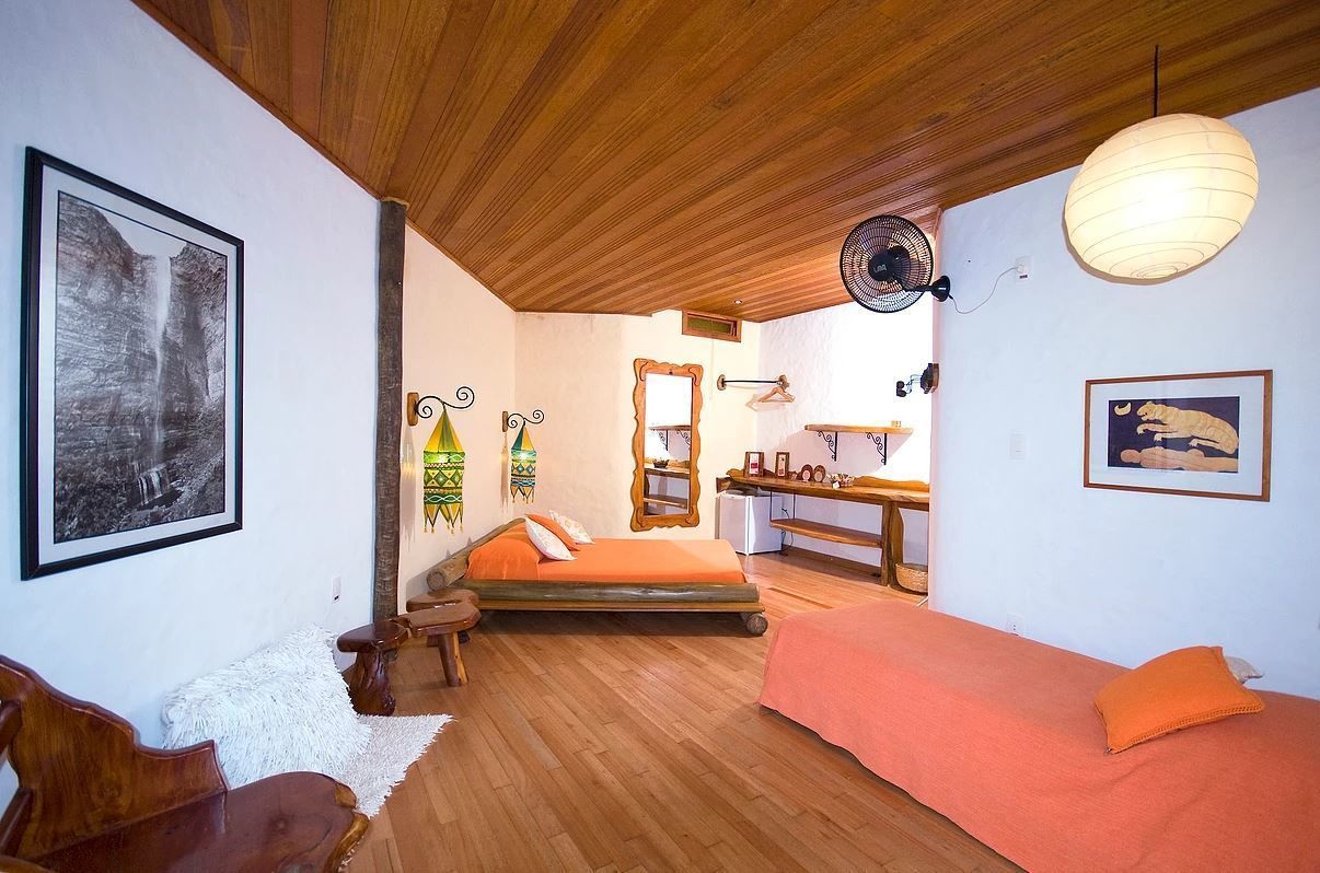 A cozy bedroom with a wooden ceiling, a bed with orange bedding, a small table, and a chair.