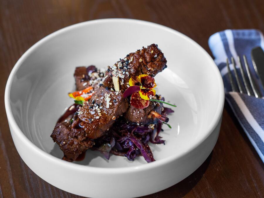 Uma tigela branca com um prato de carne e legumes, acompanhado de um garfo e um guardanapo sobre uma mesa de madeira.