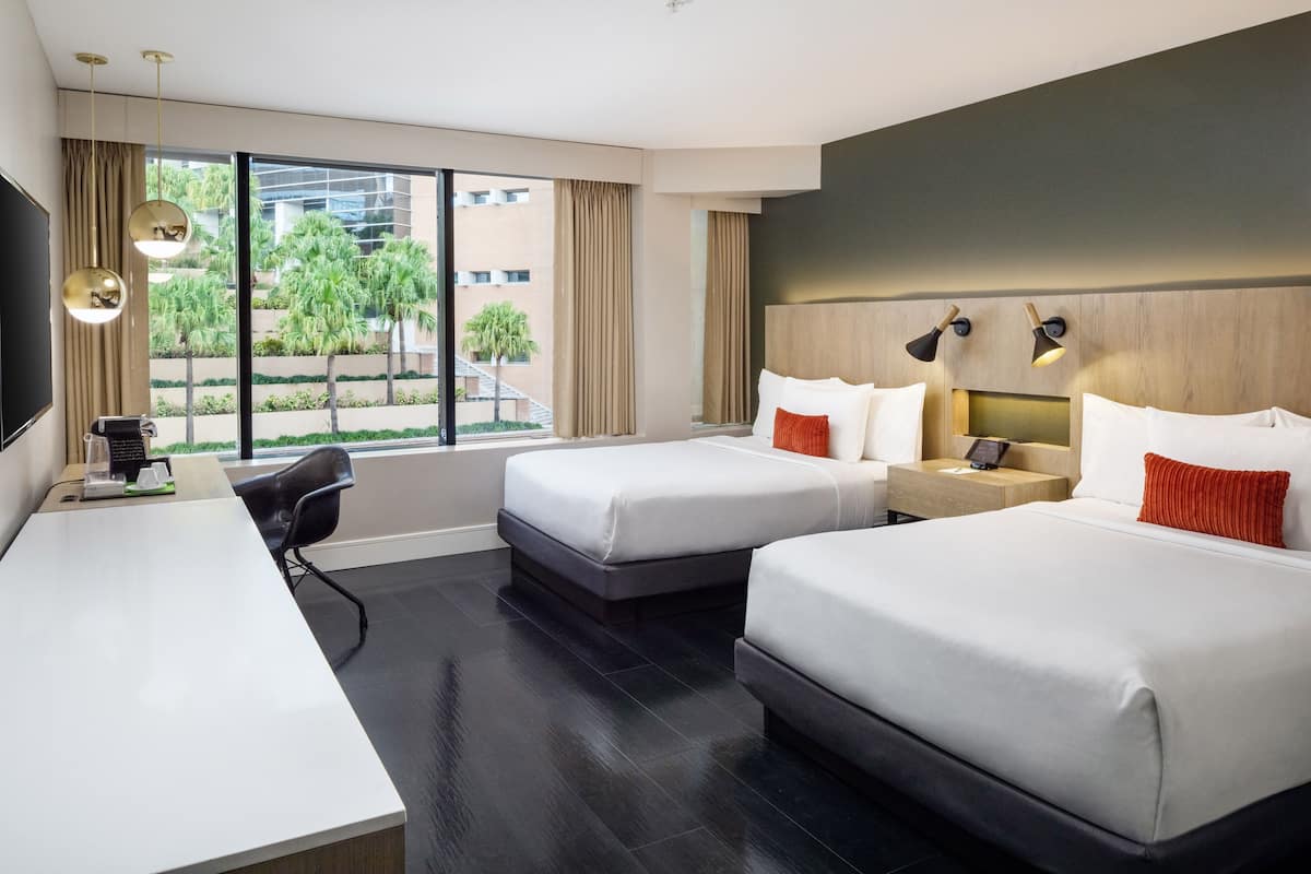 A hotel room with two beds, a desk, a chair, and a TV.