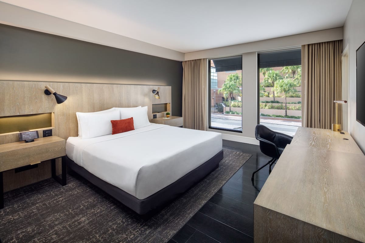 A modern hotel room with a large bed, a desk, and a view of the outdoors.
