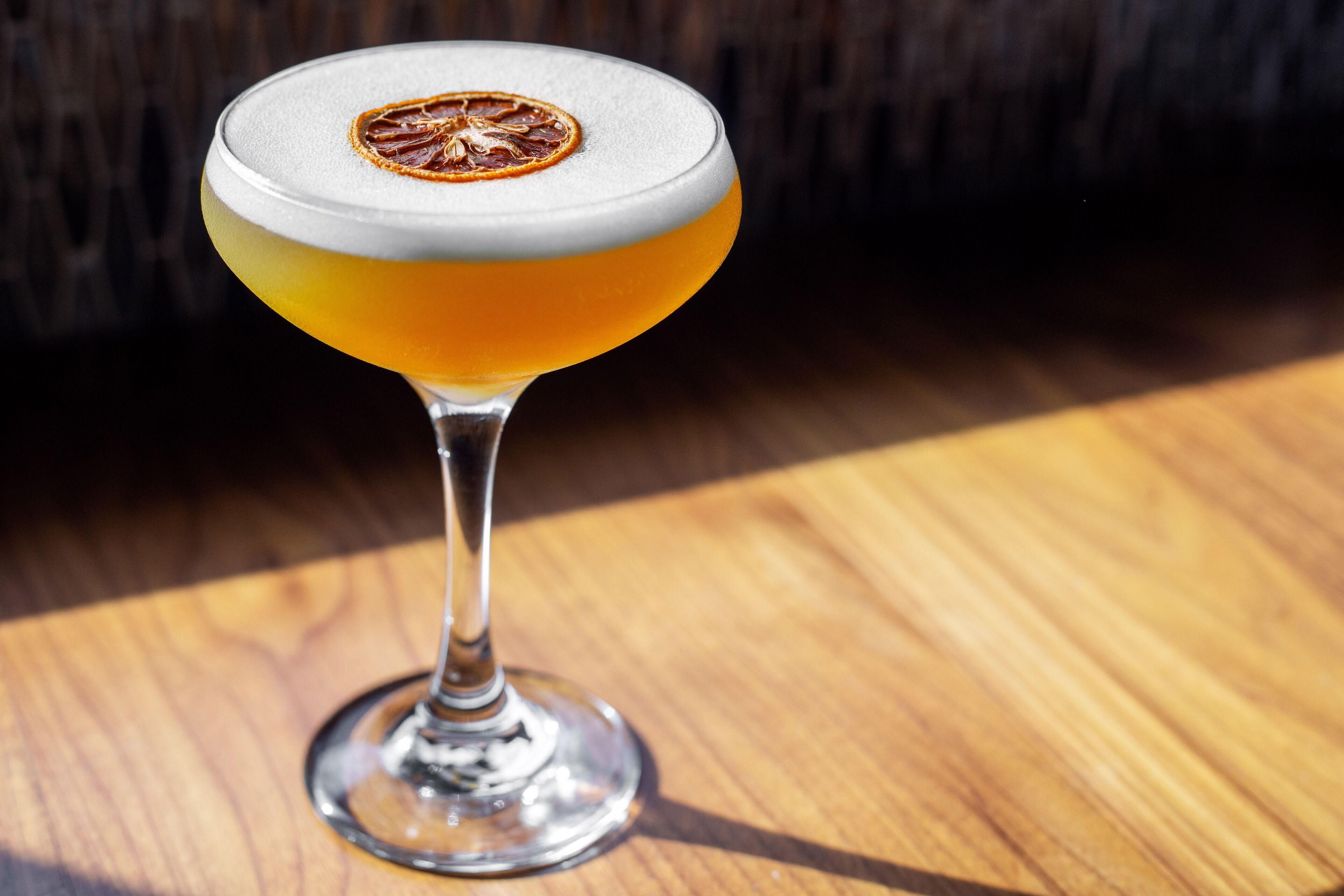A cocktail in a martini glass with a dried orange slice garnish on a wooden surface.