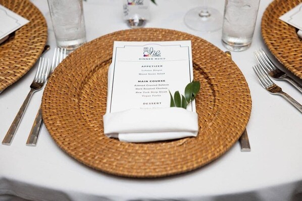 Un ambiente de comedor formal con un menú sobre un posavasos tejido, cubiertos y vasos de agua.