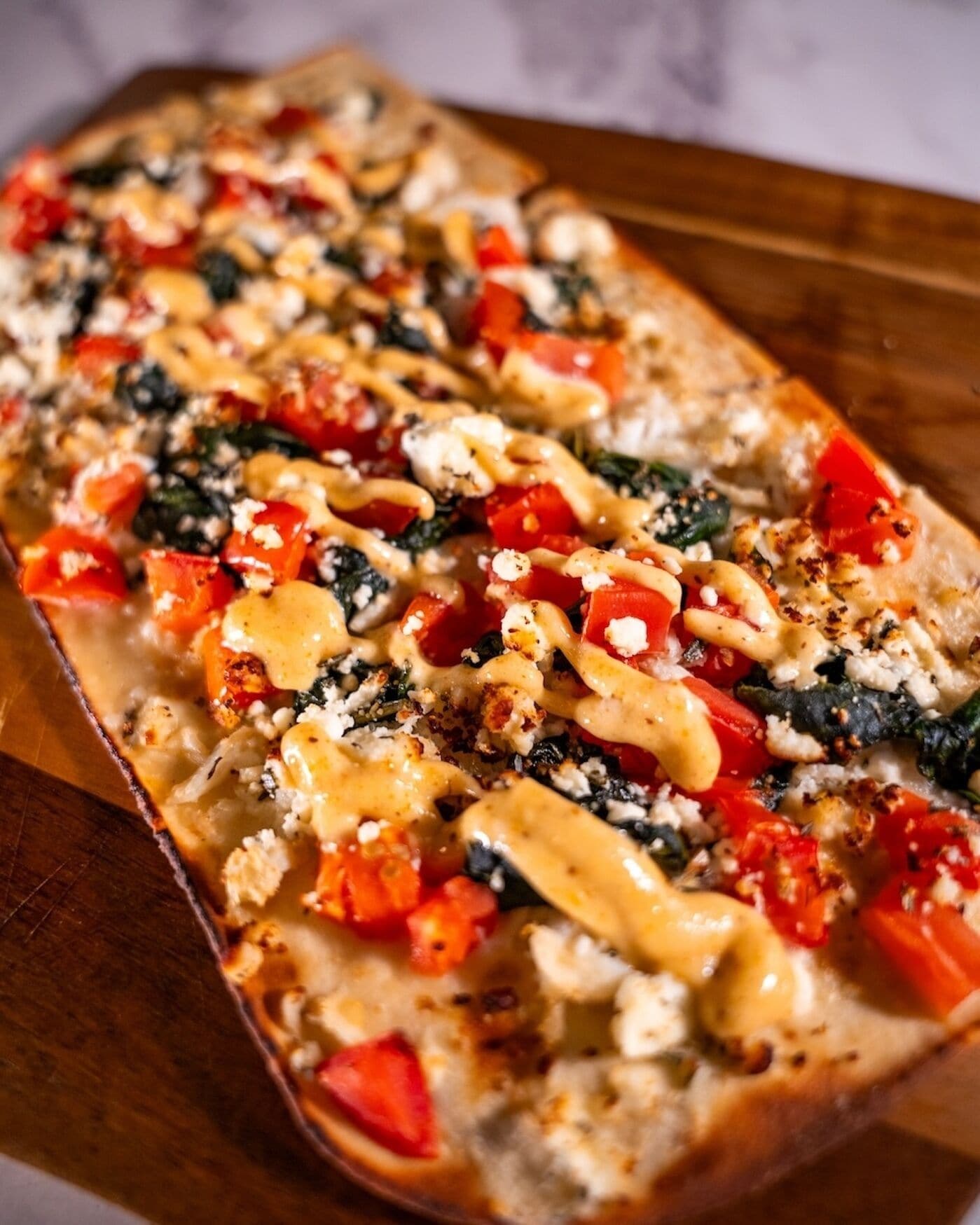 Un plat rectangulaire contenant un plat en couches, peut-être une sorte de gratin ou de plat cuit au four, recouvert de fromage, de tomates et d’une sauce crémeuse.