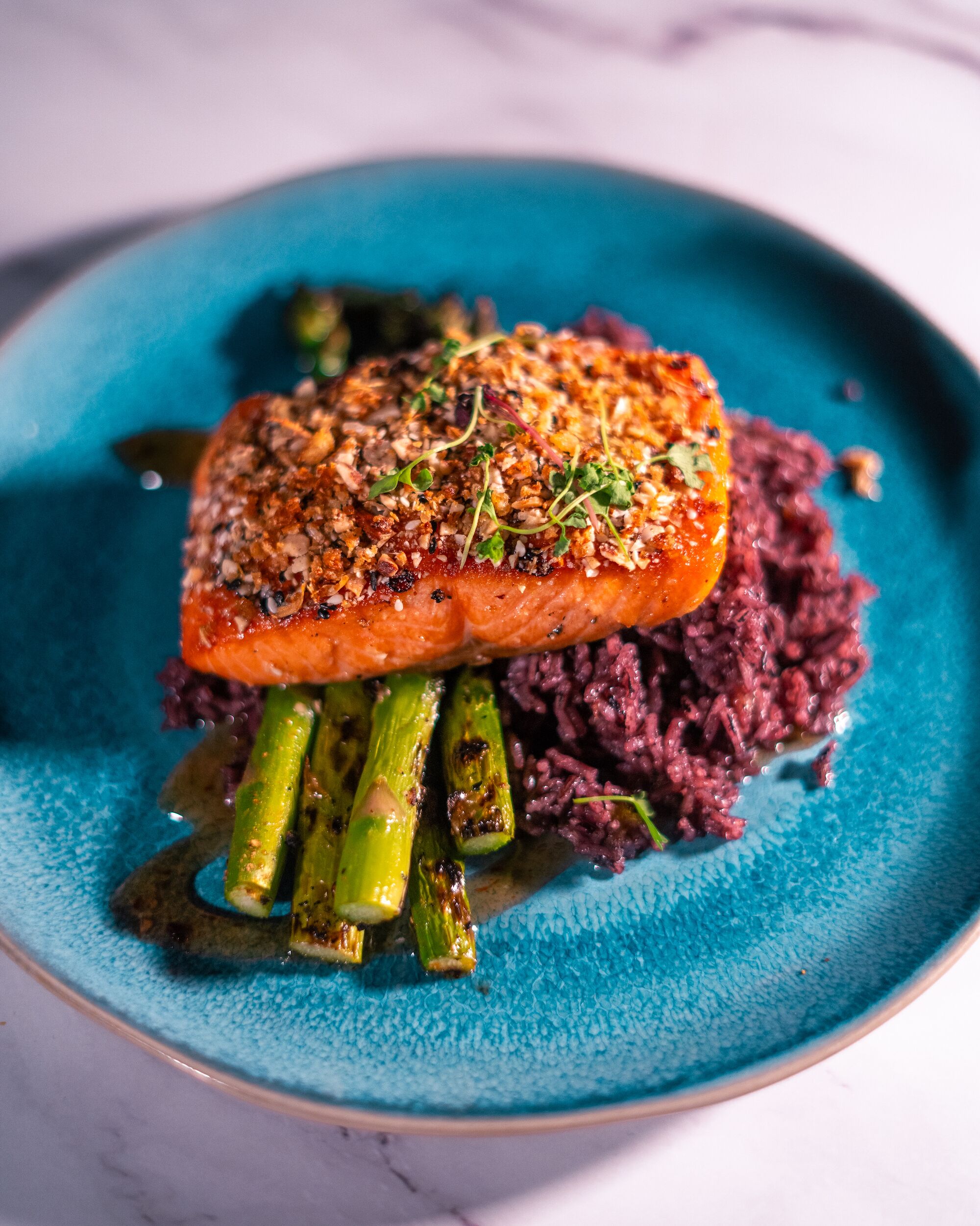 A plate with a piece of salmon, asparagus, and purple rice.