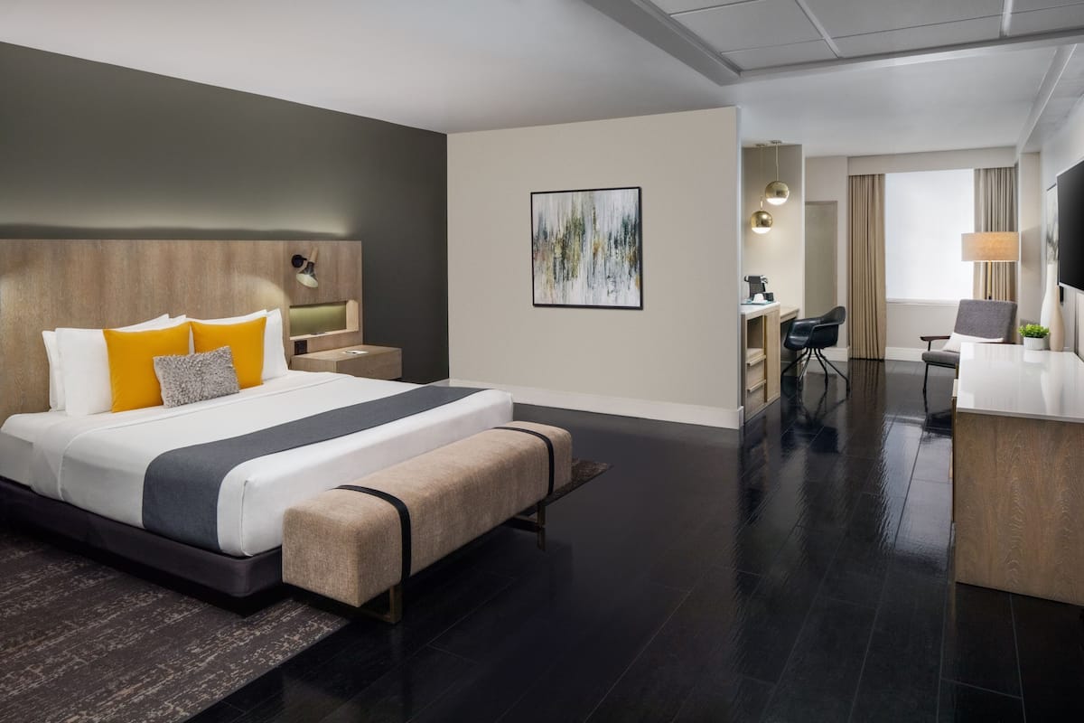 A modern hotel room with a large bed, bedside tables, a desk, a chair, and a TV.