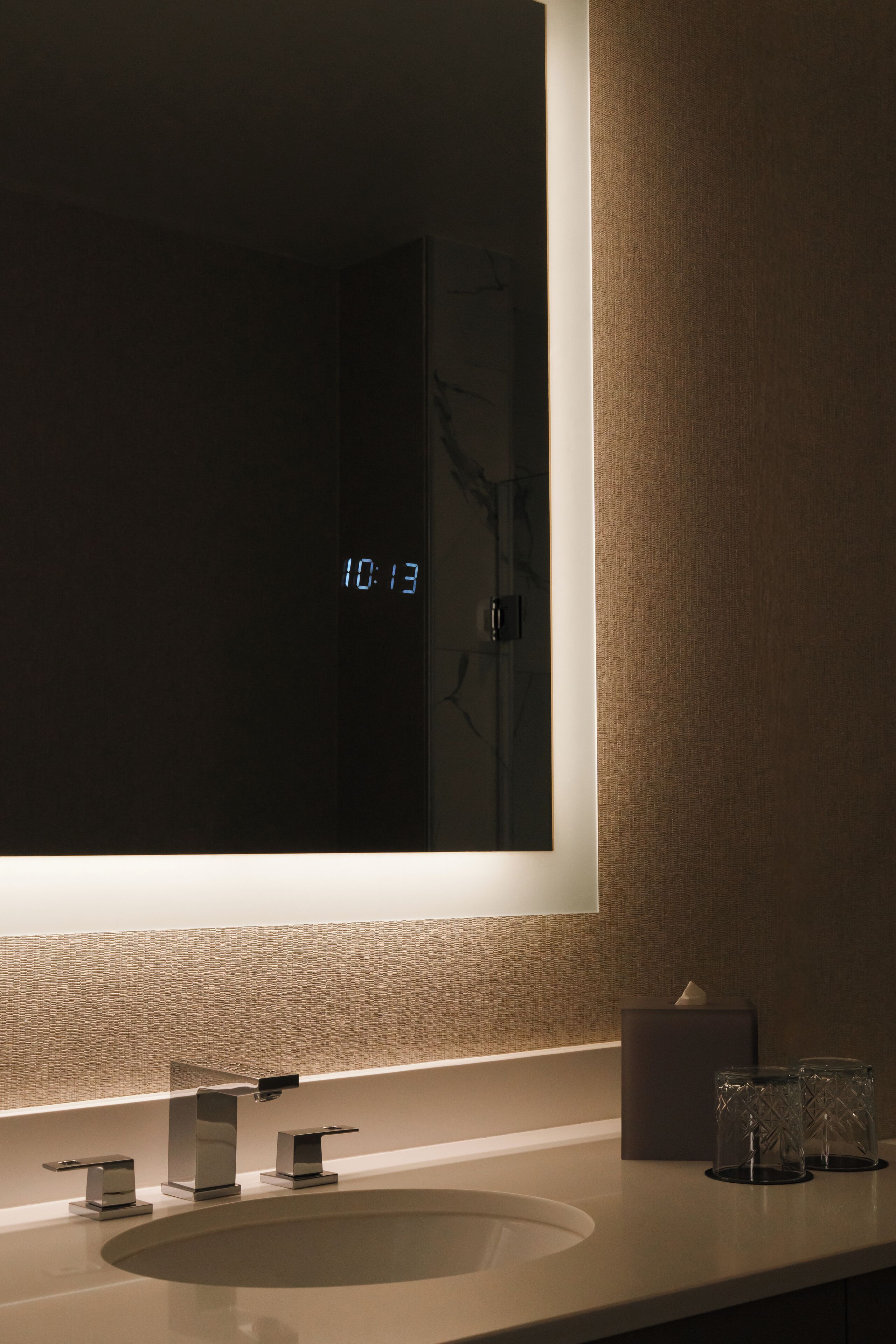 A modern bathroom with a large mirror, a sink, and a digital clock displaying 10:13.