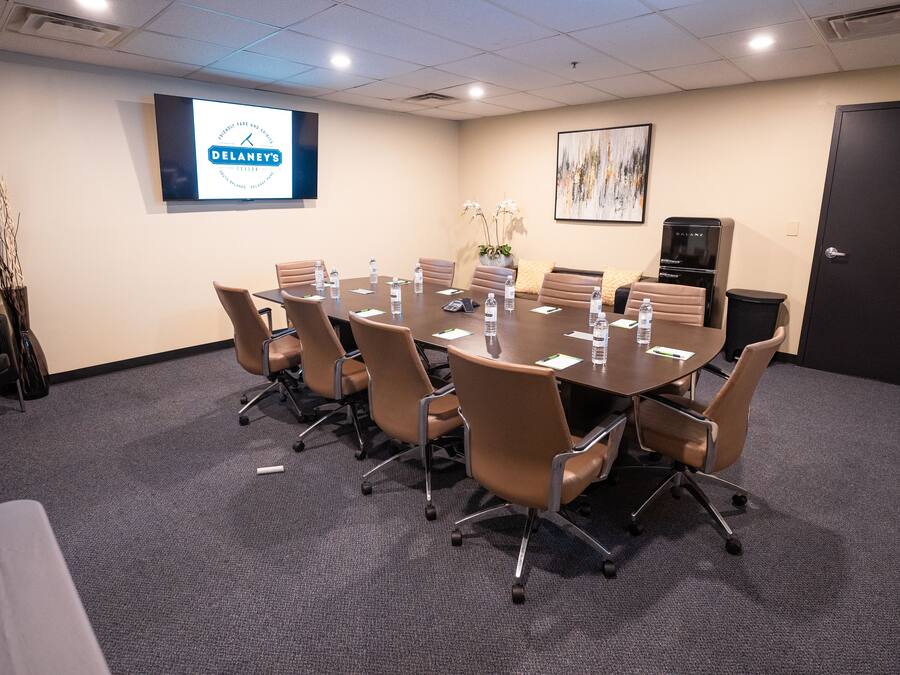 A conference room with a large table, brown chairs, a projector screen, and a Galanz refrigerator.