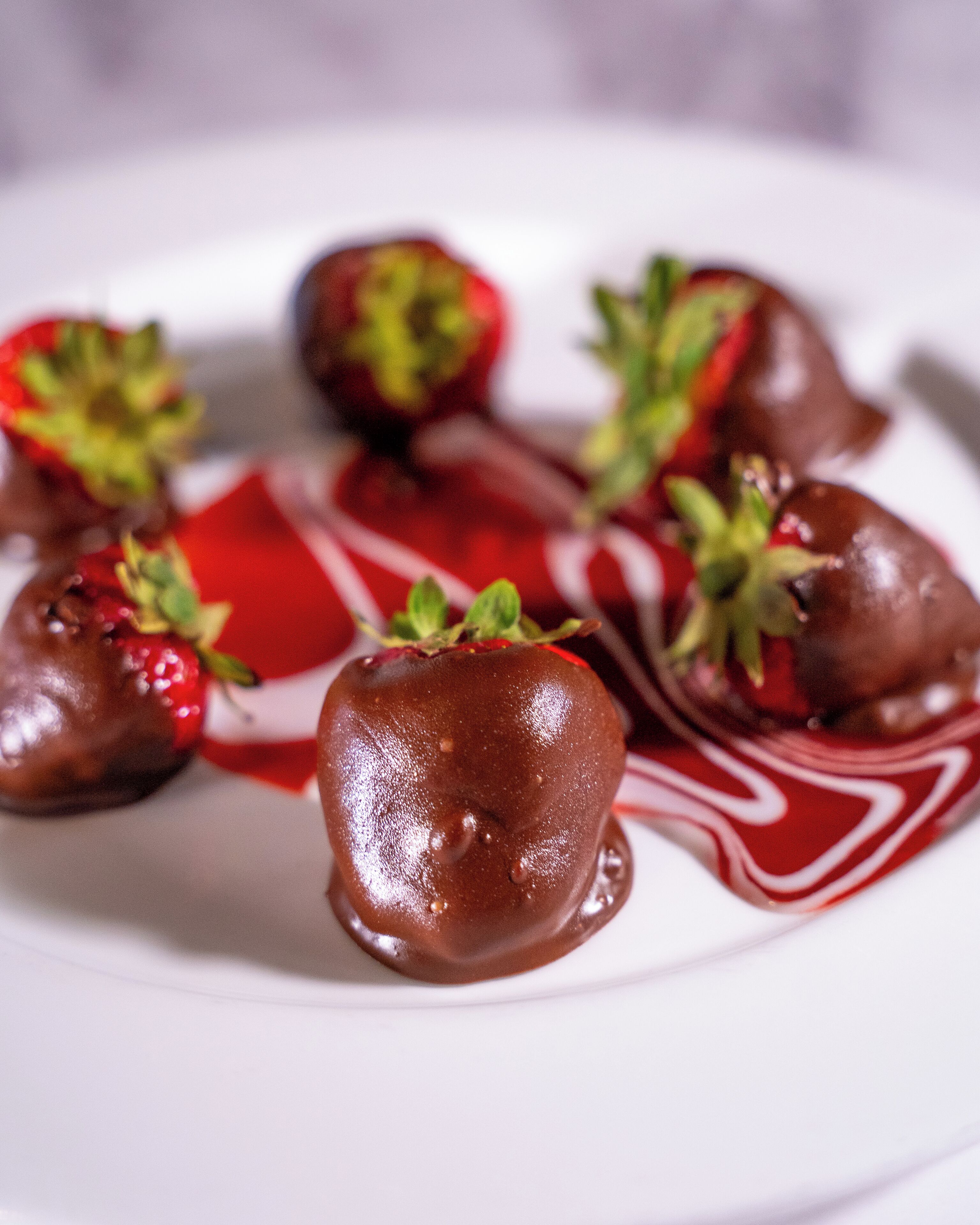 A plate with chocolate-covered strawberries and a red sauce.