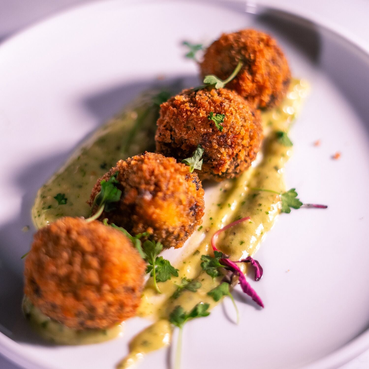 A plate of food with three round, breaded items and a green sauce.