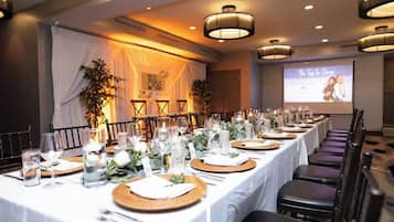 A banquet hall with a long table set for a formal event, featuring a projector screen displaying "The Top In Series" and a banner reading "The One."