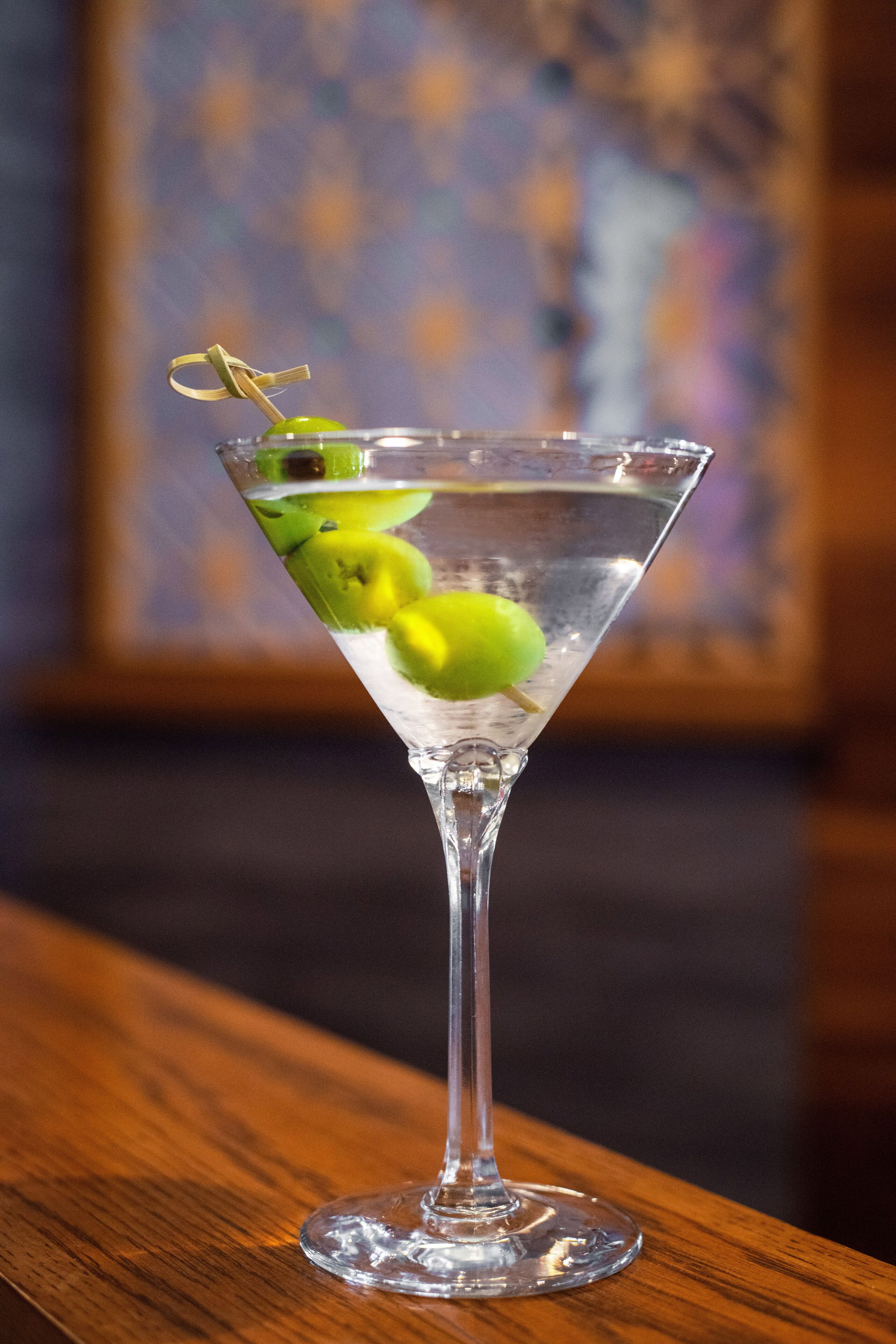 A martini glass with lime and olive garnish on a wooden surface.