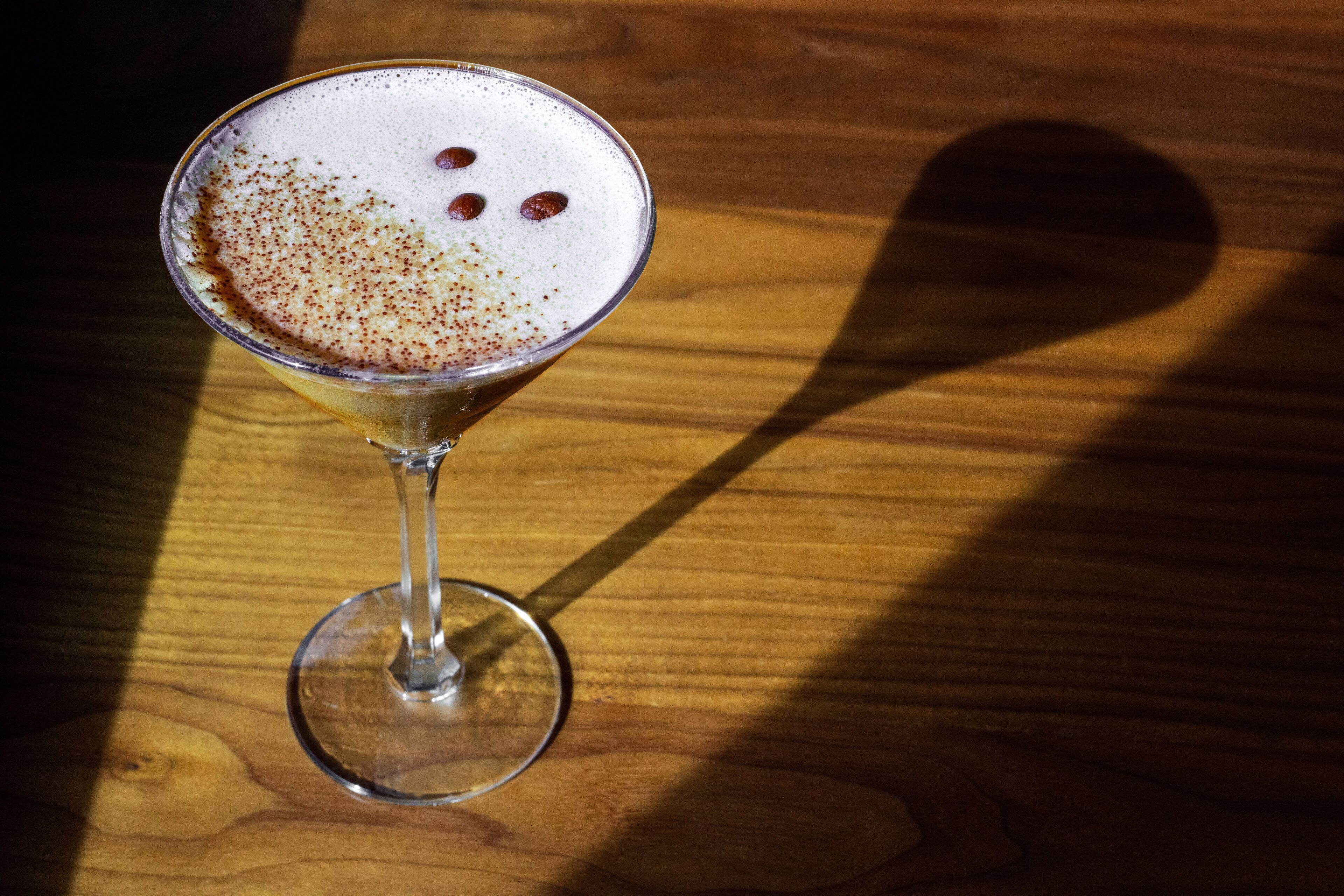 Een martini glas met een schuimige bovenkant en een beetje specerijen op een houten ondergrond.