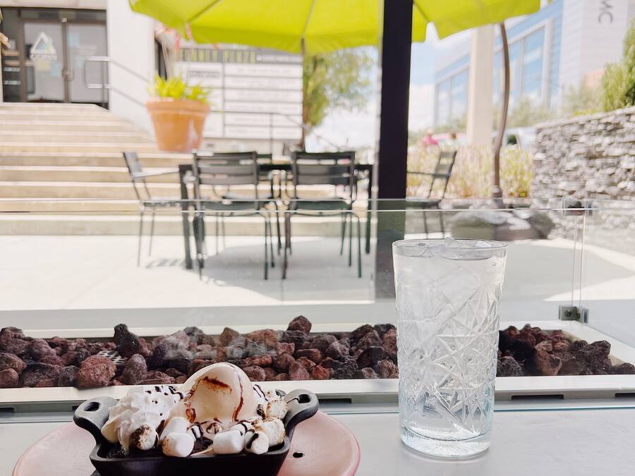 Un dessert con gelato, marshmallow e salsa al cioccolato su un piatto rosso, un bicchiere d'acqua trasparente e un ombrello verde sullo sfondo.