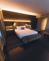Een hotelkamer met een groot bed, nachtkastjes, een bankje en een garderobe.