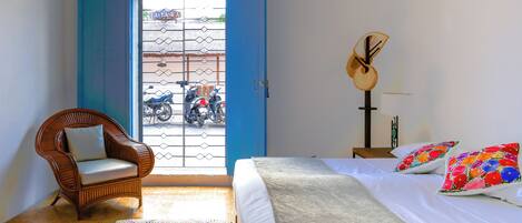 Un dormitorio con cama, una silla, una guitarra y vistas al exterior.