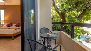 Ein Balkon mit Tisch und Stühlen, ein Bett mit Kissen und Blick auf üppiges Grün.