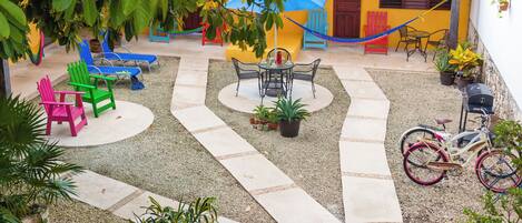A courtyard with a central seating area, surrounded by potted plants and a hammock.