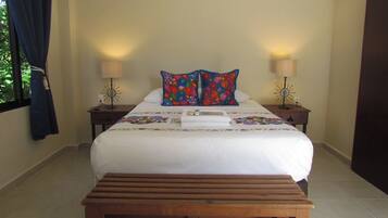 A neatly made bed with a floral quilt, two bedside lamps, and a wooden bench in front.