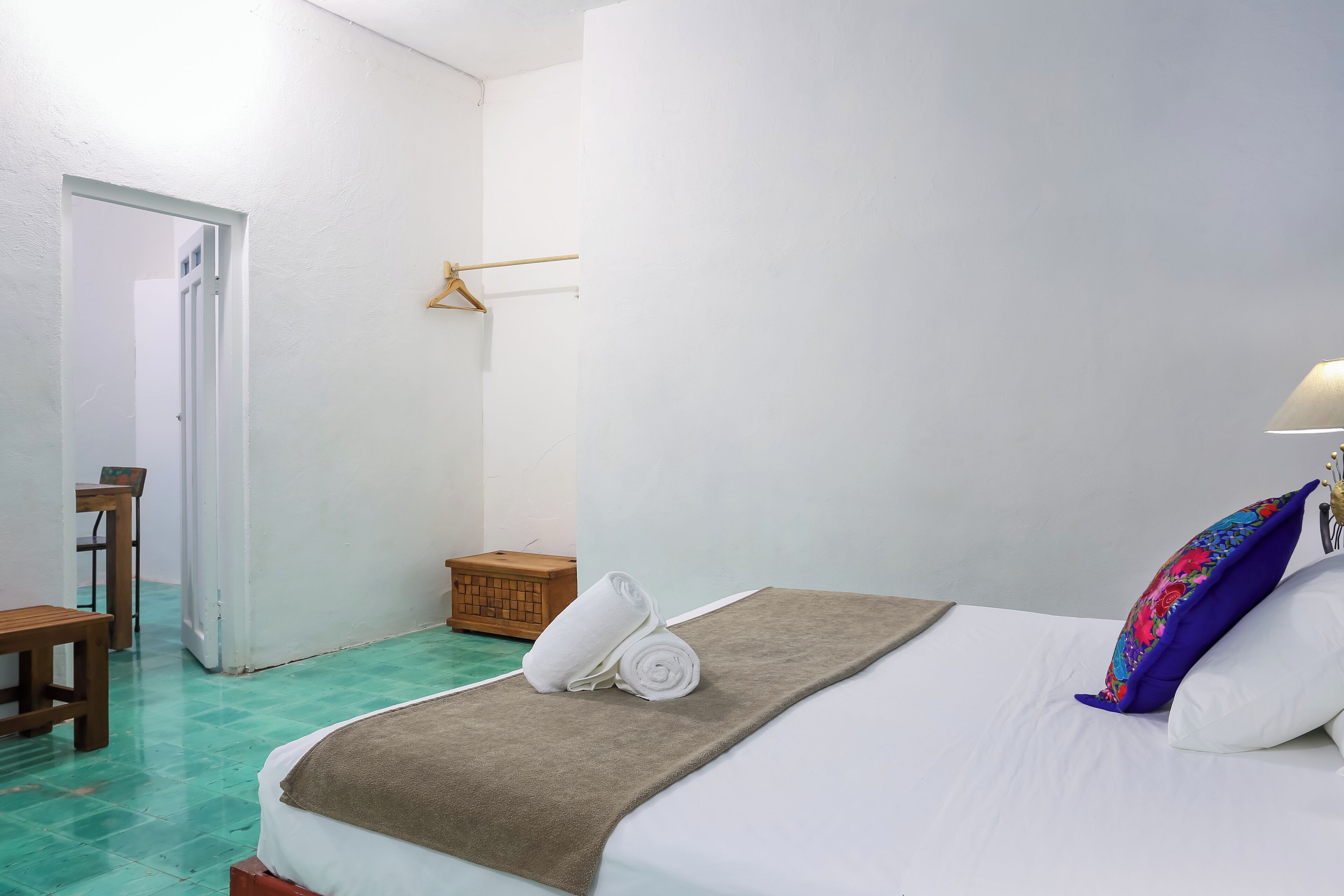 A hotel room with a bed, a wooden chair, a small wooden chest, and a hanging coat rack.