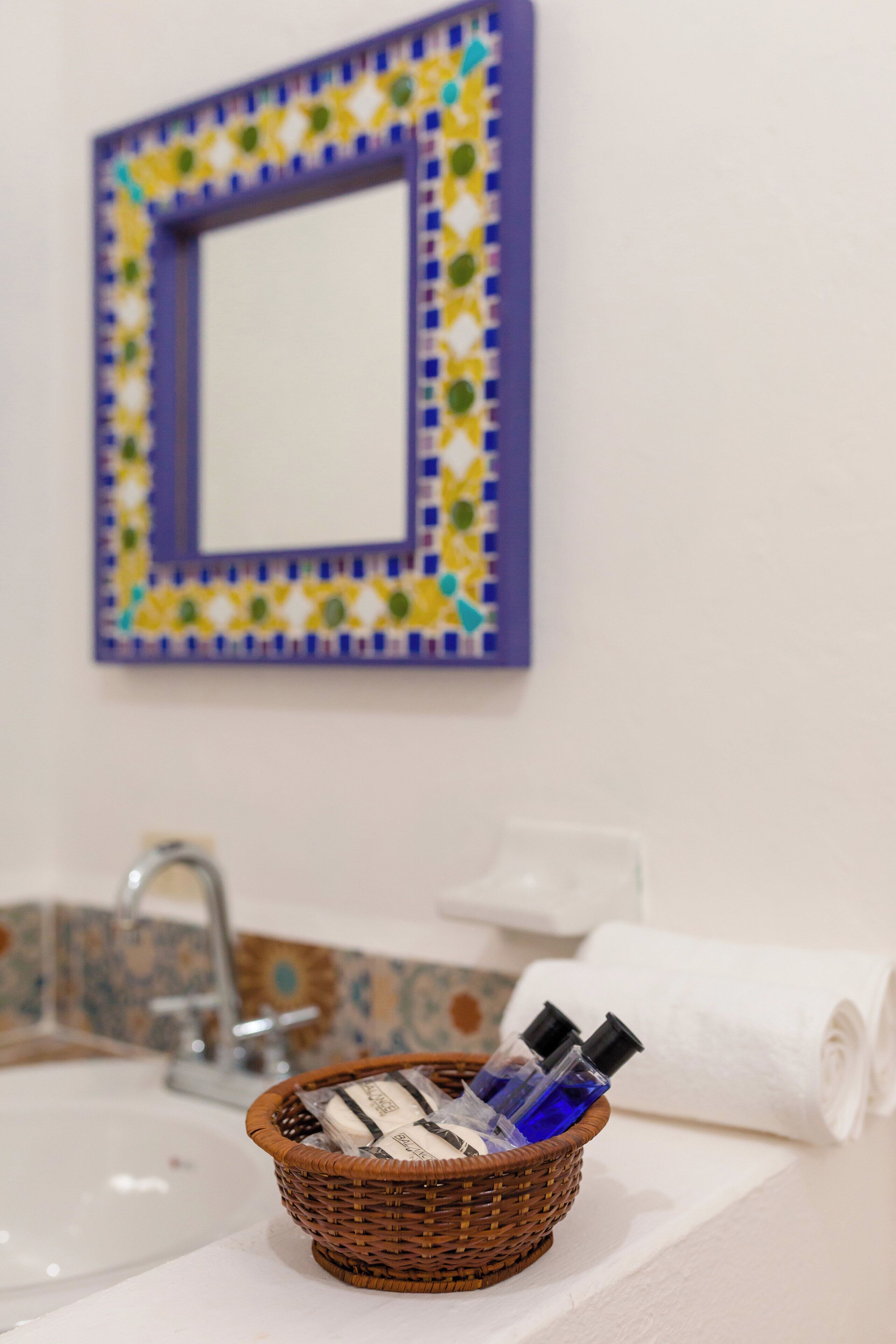 Une salle de bain avec un lavabo, un miroir doté d’un cadre coloré et un panier contenant des articles de toilette.