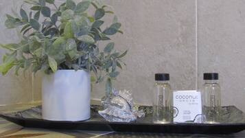 A bathroom counter with a potted plant, two bottles of coconut Grove shampoo, and a decorative item.