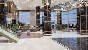 A spacious lobby with a marble staircase, seating area, and large windows offering views of the cityscape. - Hilton Istanbul Bakirkoy (Istanbul)