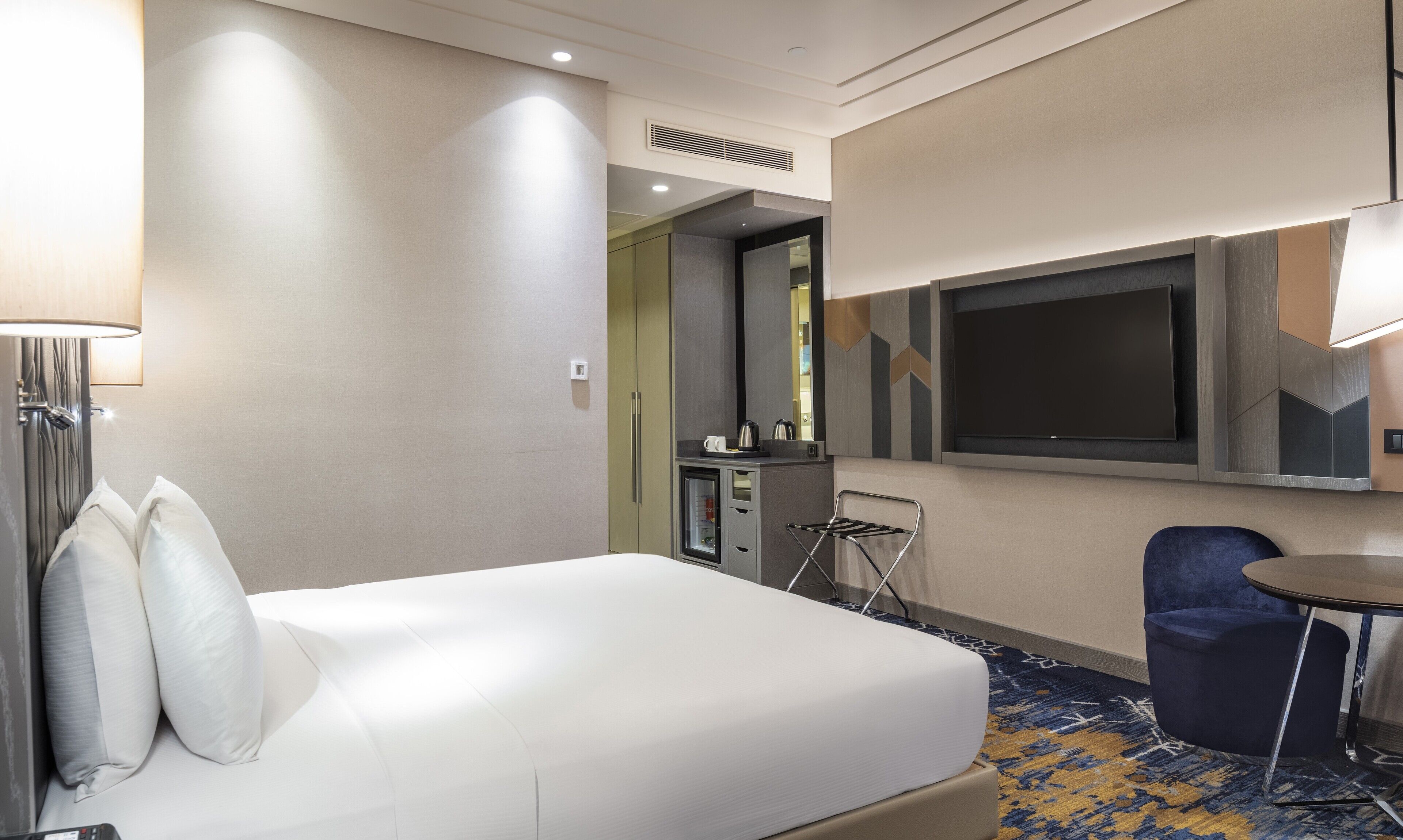 Una habitación de hotel con cama, escritorio, silla, televisor y minibar.