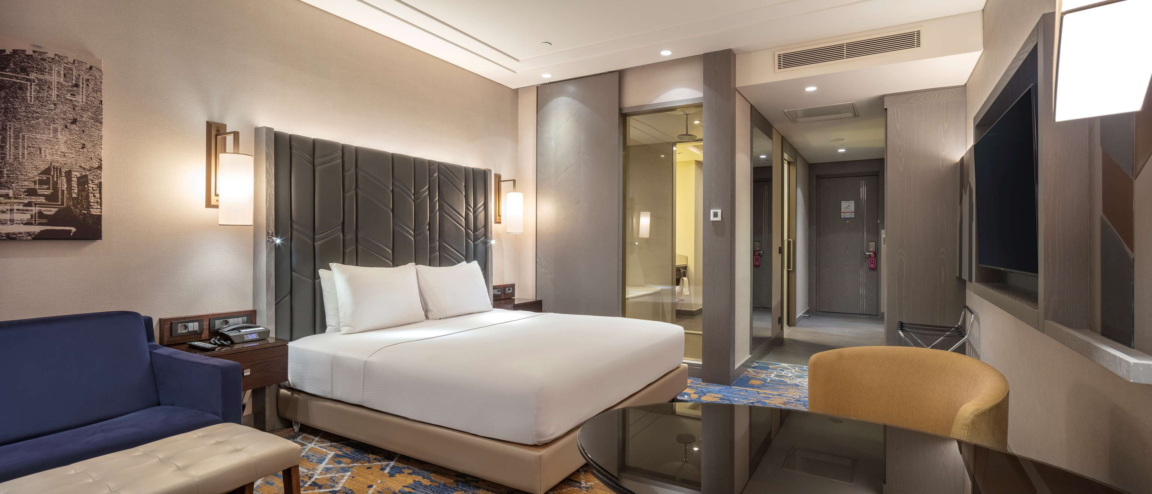 A hotel room with a large bed, a sofa, a chair, a desk, and a TV.