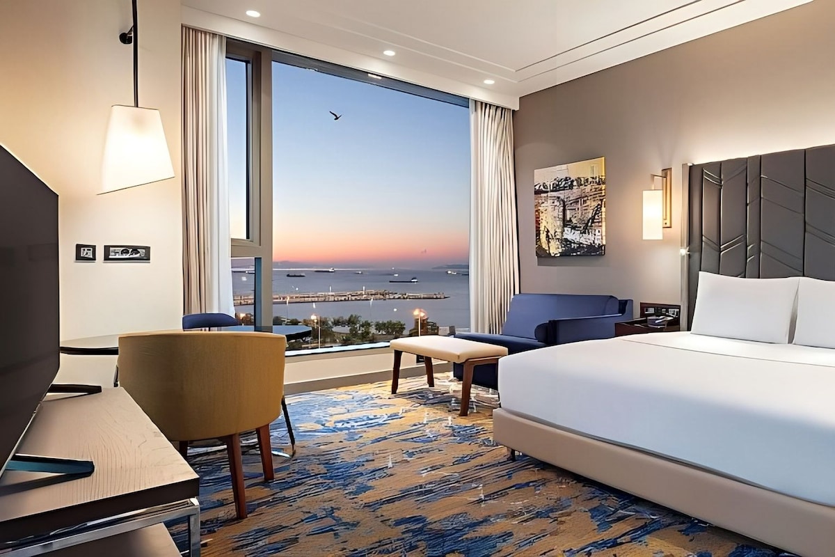 Habitación de hotel con una cama grande, un escritorio, una silla y vistas al mar.