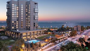 A high-rise hotel with multiple floors, a swimming pool, and a view of the sea. - Hilton Istanbul Bakirkoy (Istanbul)