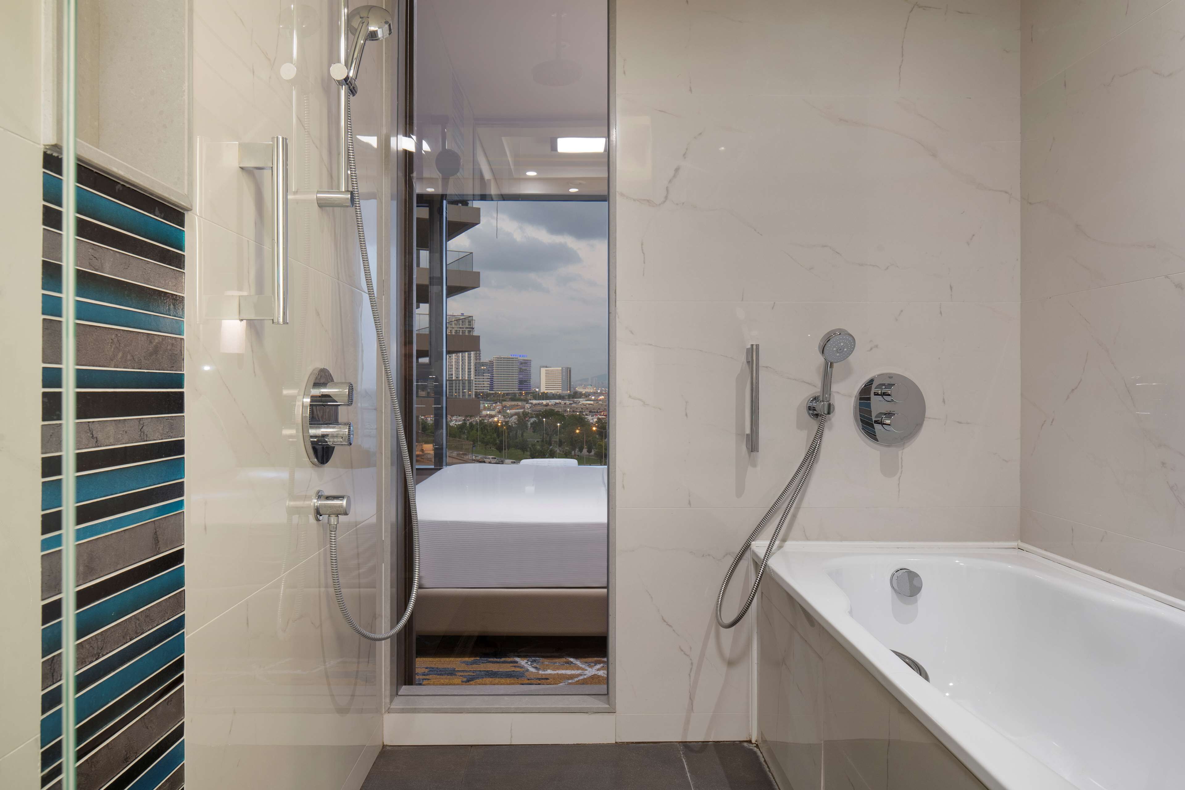 Un baño moderno con ducha, bañera y vista a la ciudad a través de una puerta de vidrio.