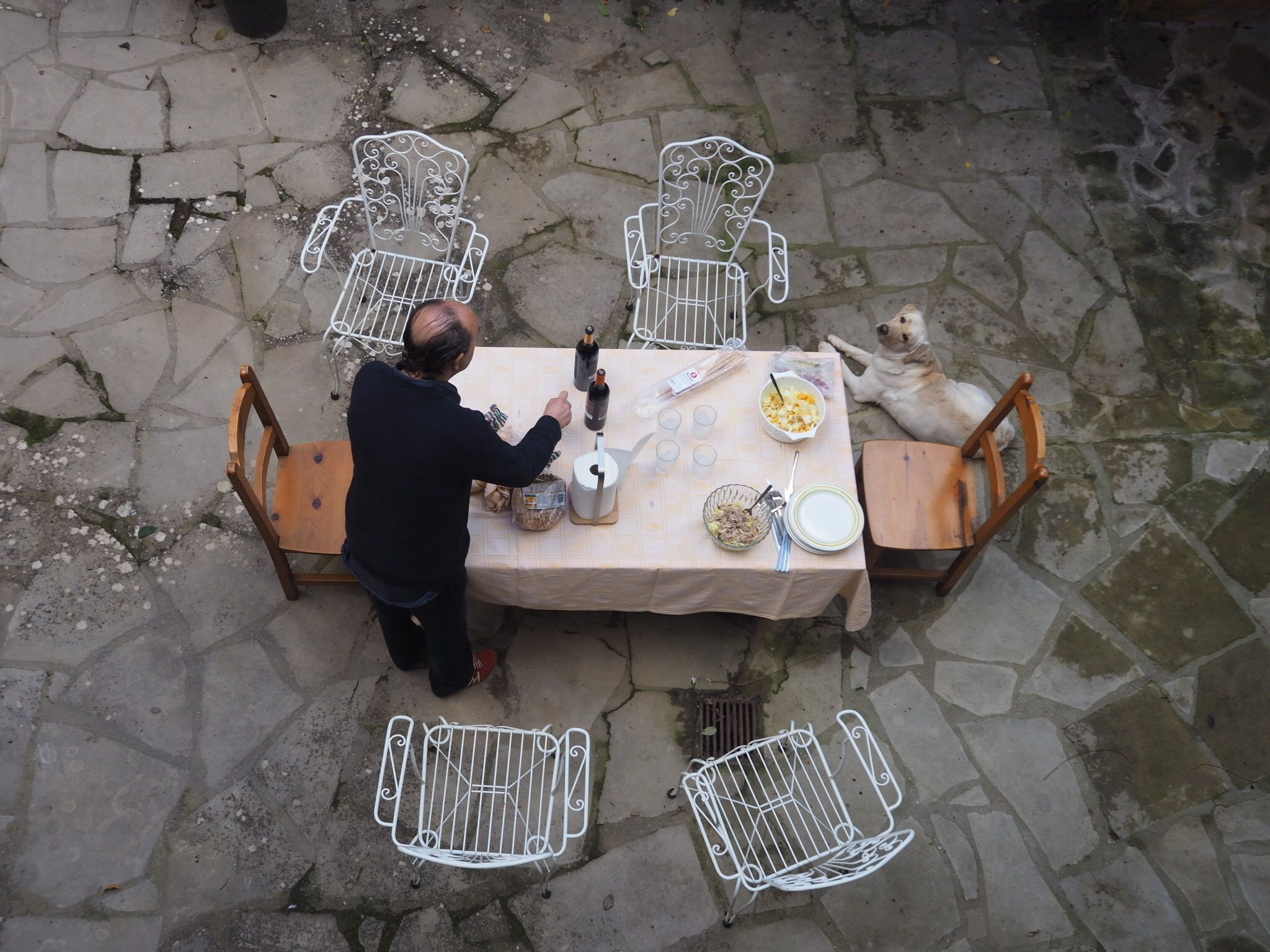A stone-paved outdoor dining area with a table set for two, surrounded by metal chairs.