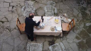 A stone-paved outdoor dining area with a table set for two, surrounded by metal chairs.