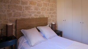 Ein Schlafzimmer mit Steinwand, einem Rattan-Kopfstück, weißer Bettwäsche und einem Nachttisch mit Kerze.