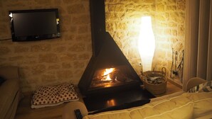 Ein gemütlicher Raum mit Kamin, einem an der Wand befestigten Fernseher und einer komfortablen Sitzecke mit Kissen und Decke.